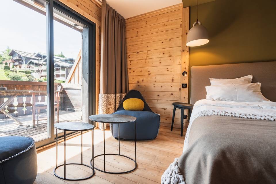 Chambre en bois clair de l'hôtel La Marmotte, lit habillé et balcon donnant sur le village des Gets